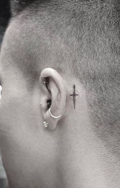 a man with a cross tattoo on his ear and behind the ear is an ear piercing