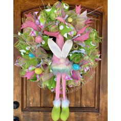 a wreath with a bunny on it hanging from the front door, decorated with green and pink decorations