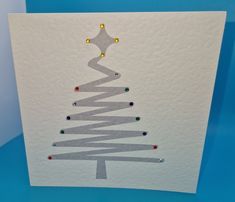 a white card with a christmas tree made out of silver foil and colored beads on it