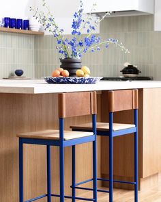 two blue stools sit in front of a kitchen island with fruit on it and flowers