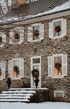 a stone house with white shutters and wreaths on the front door in winter