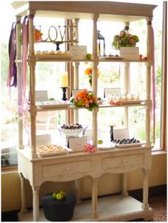 a display case with flowers and cupcakes on it in front of a window