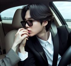 a person sitting in a car with their hand on his chin, wearing sunglasses and a suit