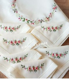 embroidered napkins with flowers and leaves on them are laid out on a wooden table