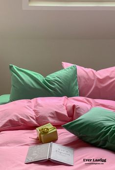 a bed with pink and green sheets, pillows and a book on the pillowcase