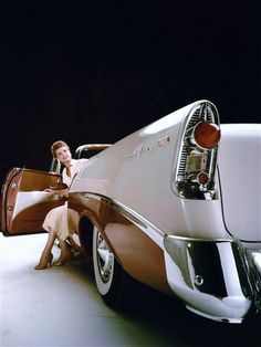 a woman sitting on the back of an old car with luggage in her hand,