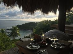 an outdoor dining area overlooking the ocean at sunset with plates and wine glasses on it