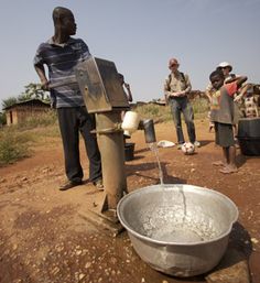 a group of people standing around a metal bucket filled with water on top of a dirt field