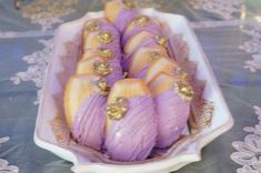 purple and gold decorated desserts in a white dish on a tablecloth with doily