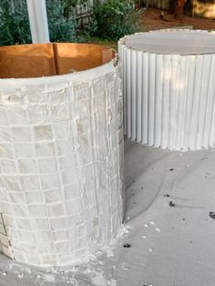 two white vases sitting next to each other on top of a cement floor covered in dirt