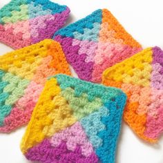 four crocheted coasters are arranged on a white surface, one is multicolored