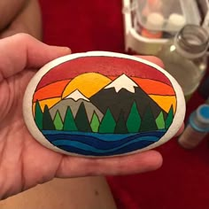 a hand holding a painted rock with mountains in the background