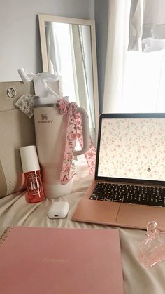 an open laptop computer sitting on top of a bed next to a pink vase and other items