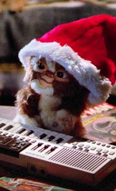 a small cat wearing a santa hat sitting next to a remote control on top of a table