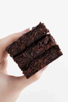 a hand holding three pieces of brownie in it's left hand on a white background