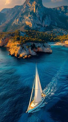 an aerial view of a sailboat sailing in the ocean with mountains in the background