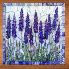 a stained glass panel with purple flowers in it on a wooden table next to a window