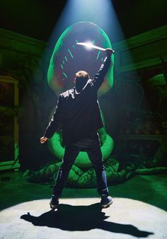 a man standing in front of a giant green object with a light on it's head