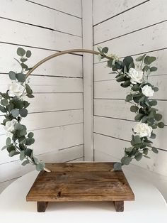 a wooden tray with white flowers and greenery in the shape of a circle on it