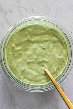 a glass bowl filled with green sauce next to a wooden spoon on a marble surface