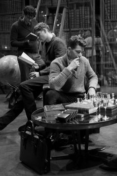 black and white photo of men playing chess in front of bookshelves with wine glasses