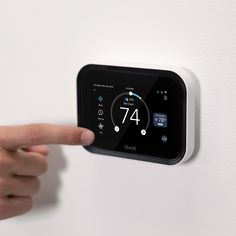 a person pointing at thermostaer on a wall