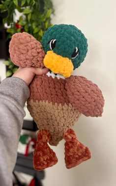 a person holding a stuffed animal in their hand with a green and brown bird on it's head