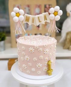 a pink cake decorated with white flowers and buntings is sitting on a table