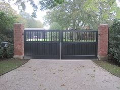 an iron gate with brick pillars is shown in front of some bushes and trees on the other side