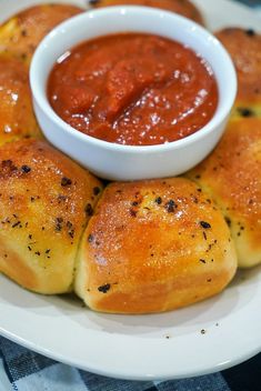 some bread rolls are on a white plate with a small bowl of sauce in the middle