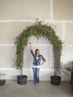 a woman standing next to two potted plants in front of a wall with vines on it