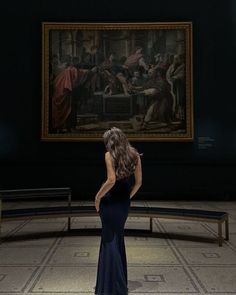 a woman in a black dress looking at a painting