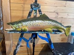 a large fish sitting on top of a blue easel next to a wooden wall