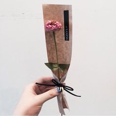 a person holding a flower wrapped in brown paper and tied to a string with a black ribbon