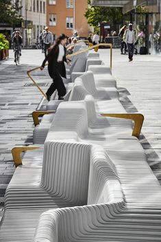 people are walking on the sidewalk with benches lined up along the curb and in front of them