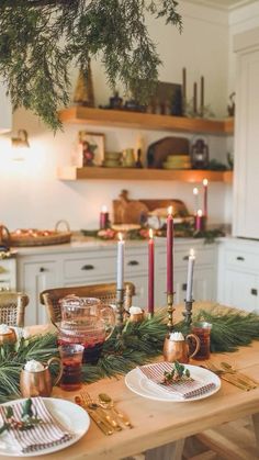 the table is set for christmas dinner with candles and greenery in front of it