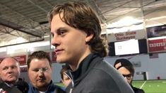 a man is talking to the media at a football game with other men in the background