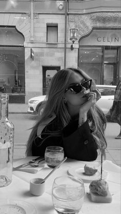 a woman sitting at a table with food and drinks in front of her, wearing sunglasses