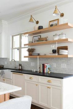 a kitchen with white cabinets and black counter tops, gold pulls on the wall shelves