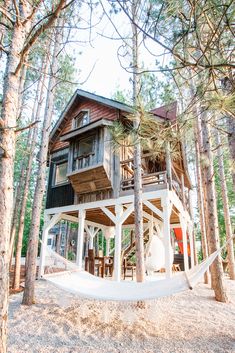 a hammock hanging from the side of a wooden house in the woods with trees around it