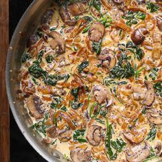 a pan filled with mushrooms and spinach on top of a stovetop next to a wooden table