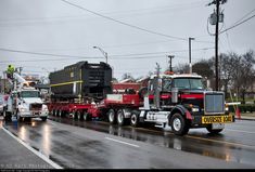 two semi trucks driving down the road with other vehicles behind them on a rainy day