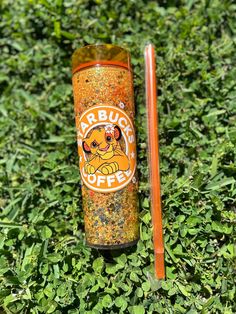 an orange cup sitting on top of a lush green field next to a red straw