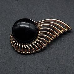 This vintage abstract black and gold tone brooch features an art deco design in gold tone with a black acrylic cabochon. It measures 2.25" W x 1.25" H. Art Deco Formal Oval Brooches, Art Deco Oval Brooch Jewelry, Art Deco Oval Cabochon Collectible Jewelry, Luxury Art Deco Brooches With Cabochon, Antique Gold Brooch With Cabochon Detail, Abstract Jewelry, Art Deco Brooch, Black Acrylics, Art Deco Design