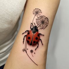 a ladybug tattoo on the arm with dandelions