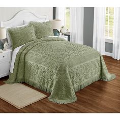 a bed with a green bedspread and pillows on top of wooden flooring