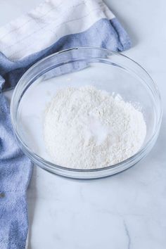 a glass bowl filled with flour on top of a white marble counter next to a blue towel