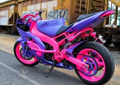 a pink and purple motorcycle parked on the side of the road next to train tracks