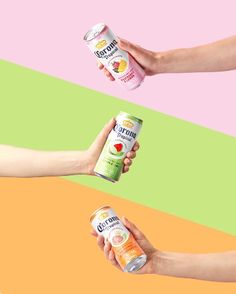 three people holding cans of fruit juice in their hands against a multi - colored background