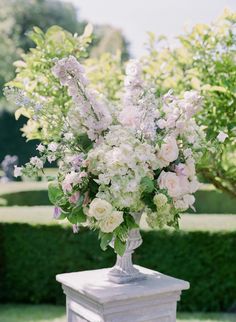 a vase filled with white and pink flowers on top of a table next to hedges